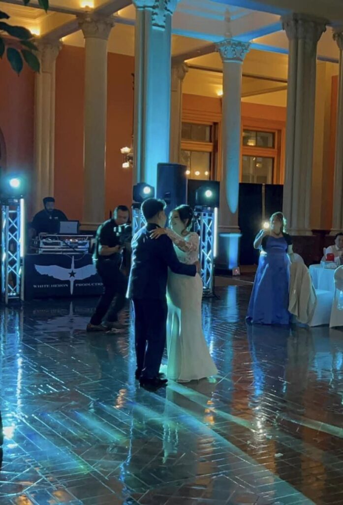 A newlywed couple shares their first dance at an elegant wedding reception in Minneapolis with a DJ in the background and guests watching